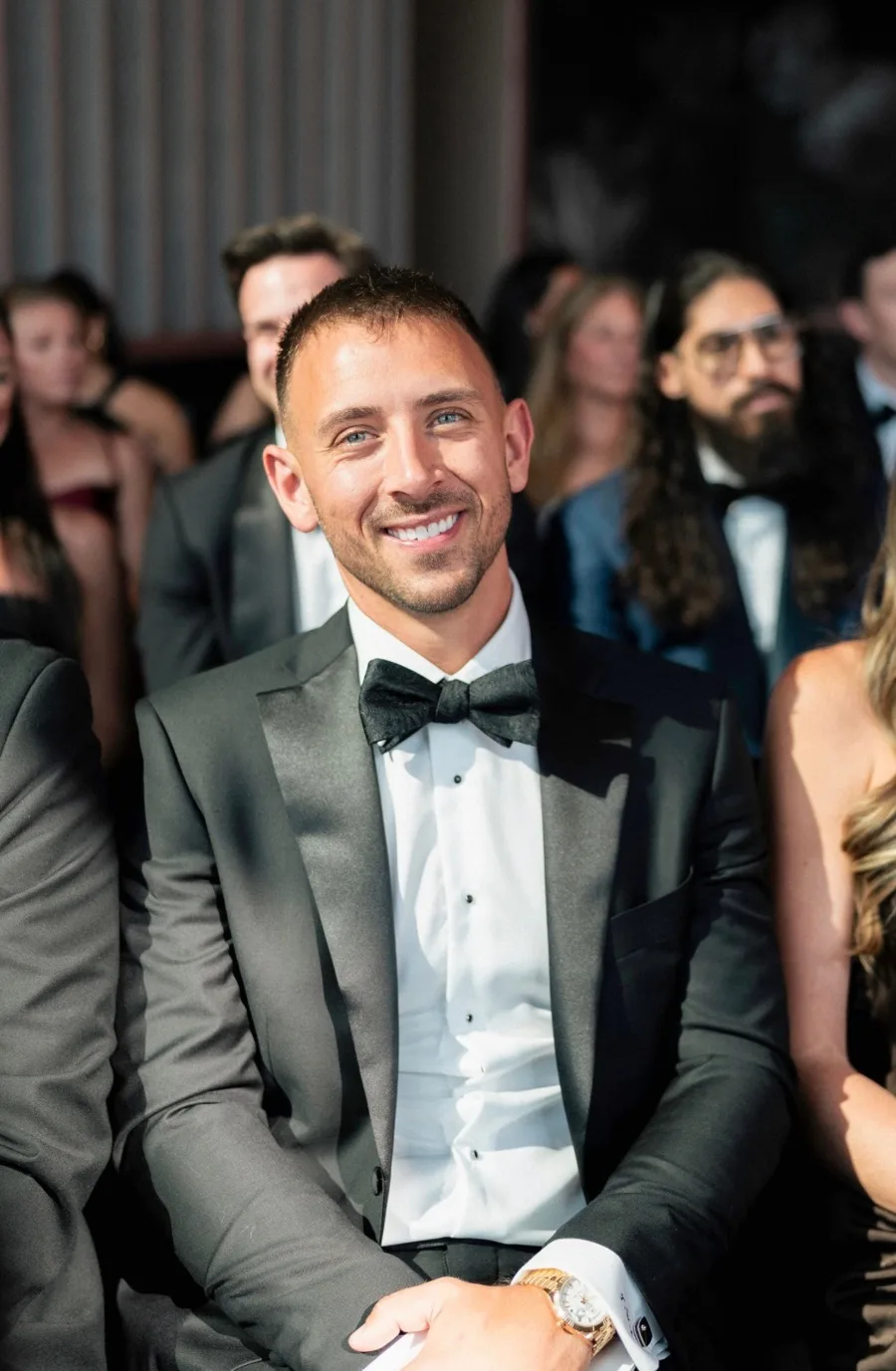 A client seated among guests at a reception in a made to measure tuxedo.