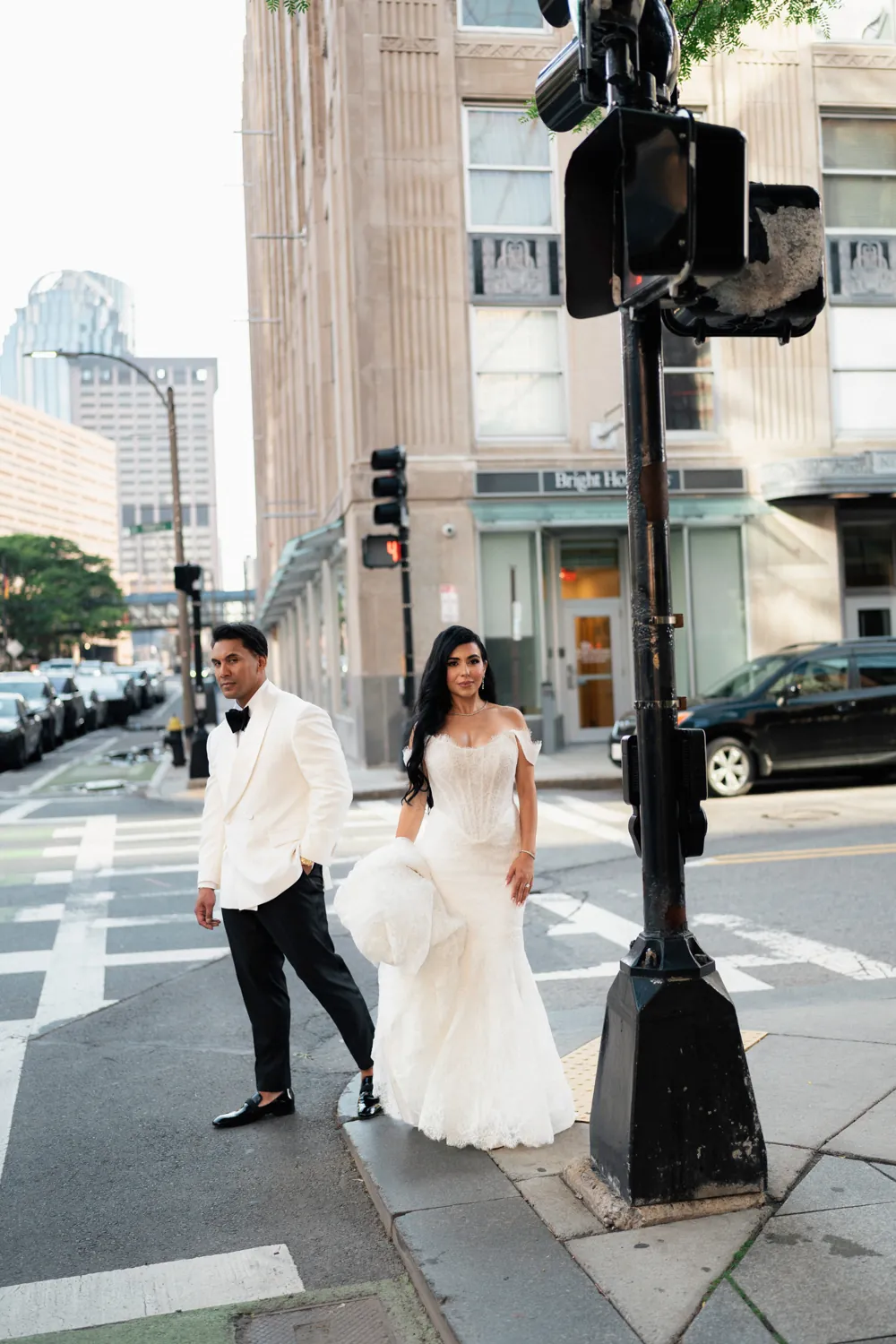 A groom in a white dinner jacket crossing a Boston street with the bride.