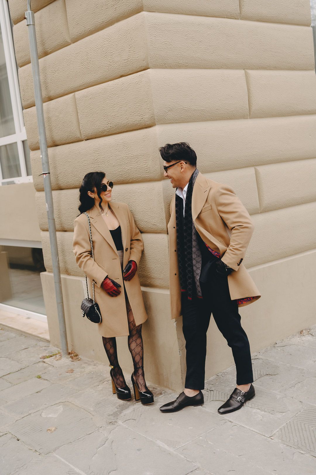 Doug and Natalie in camel overcoats against a rusticated stone wall in Florence.